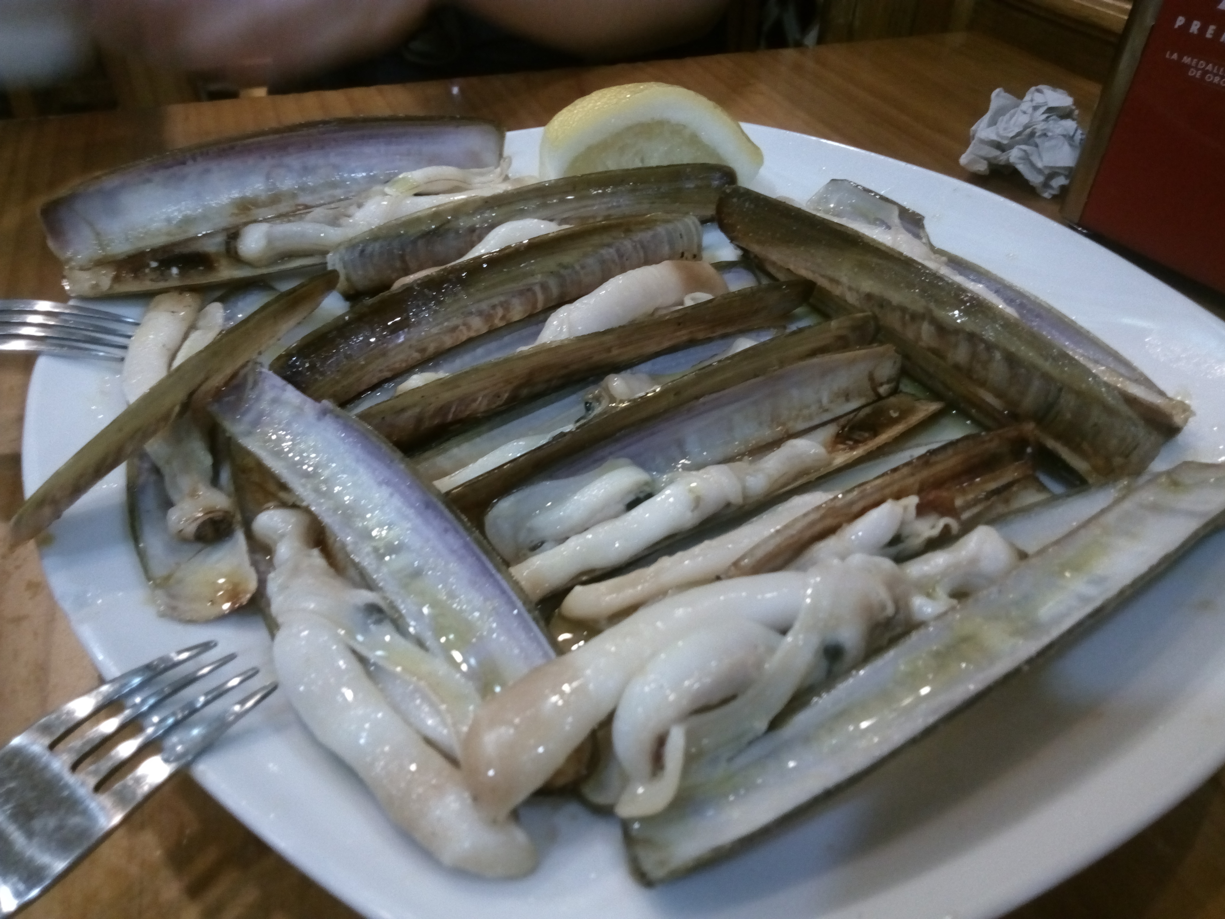 白い皿に並んだマテ貝の鉄板焼き。レモンが添えられている